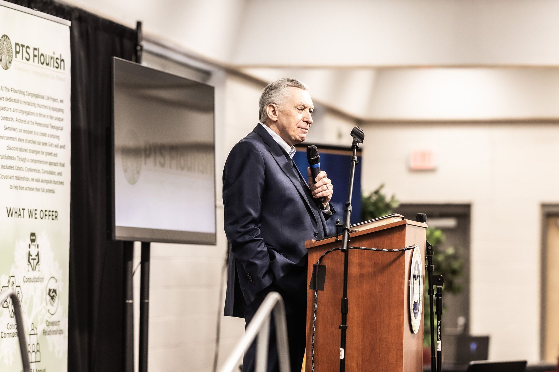 A man in a suit is standing at a podium holding a microphone.