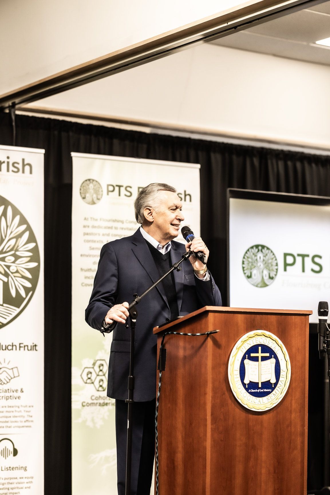 A man in a suit is standing at a podium holding a microphone.
