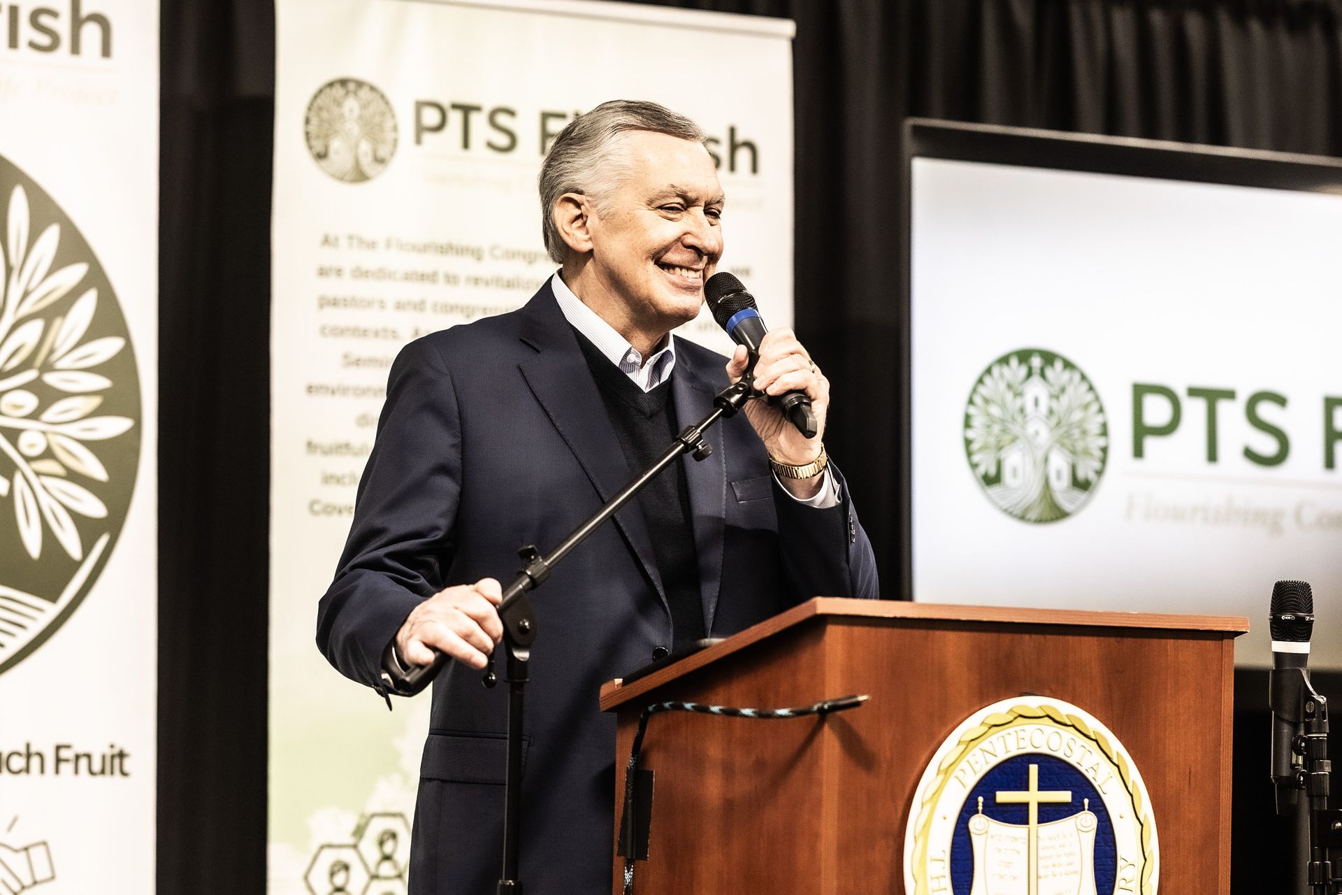 A man in a suit is standing at a podium holding a microphone.