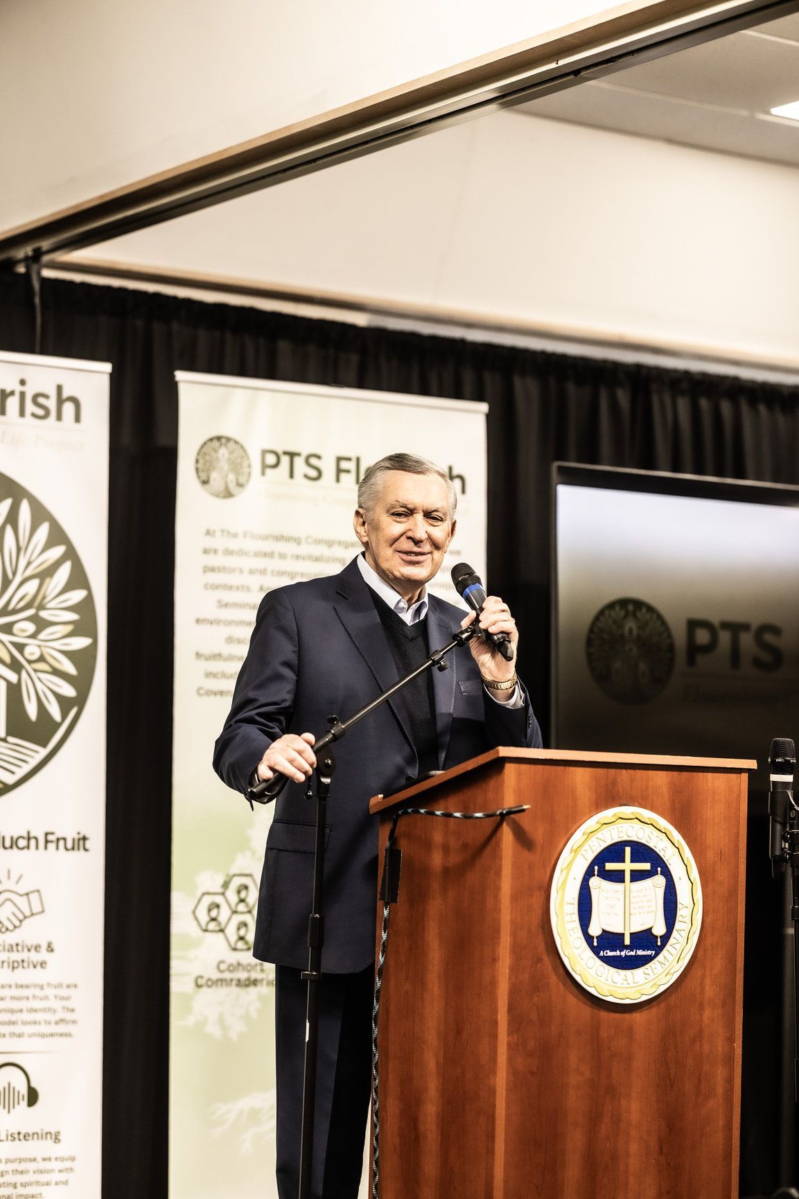 A man in a suit is standing at a podium holding a microphone.