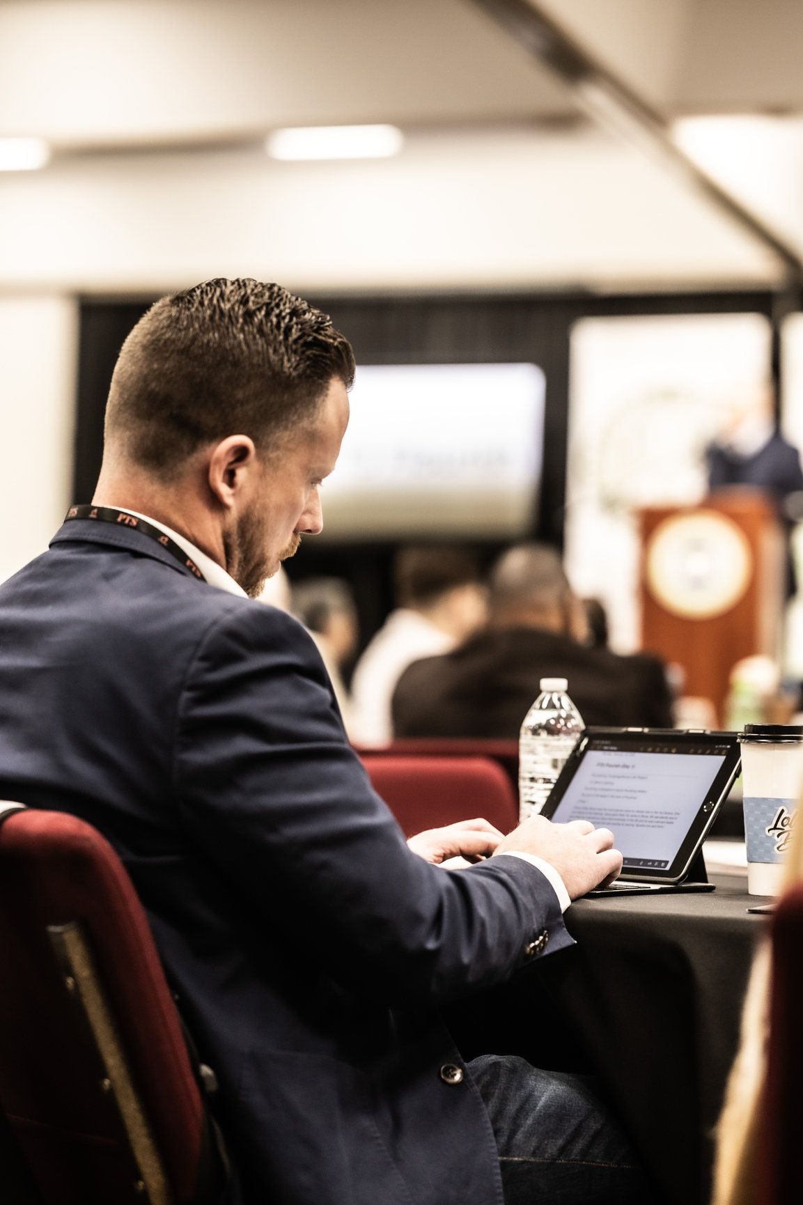 A man in a suit is sitting at a table using a tablet computer.