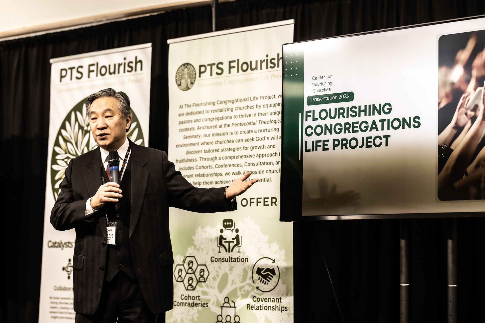 A man in a suit is standing in front of a sign that says pts flourish.