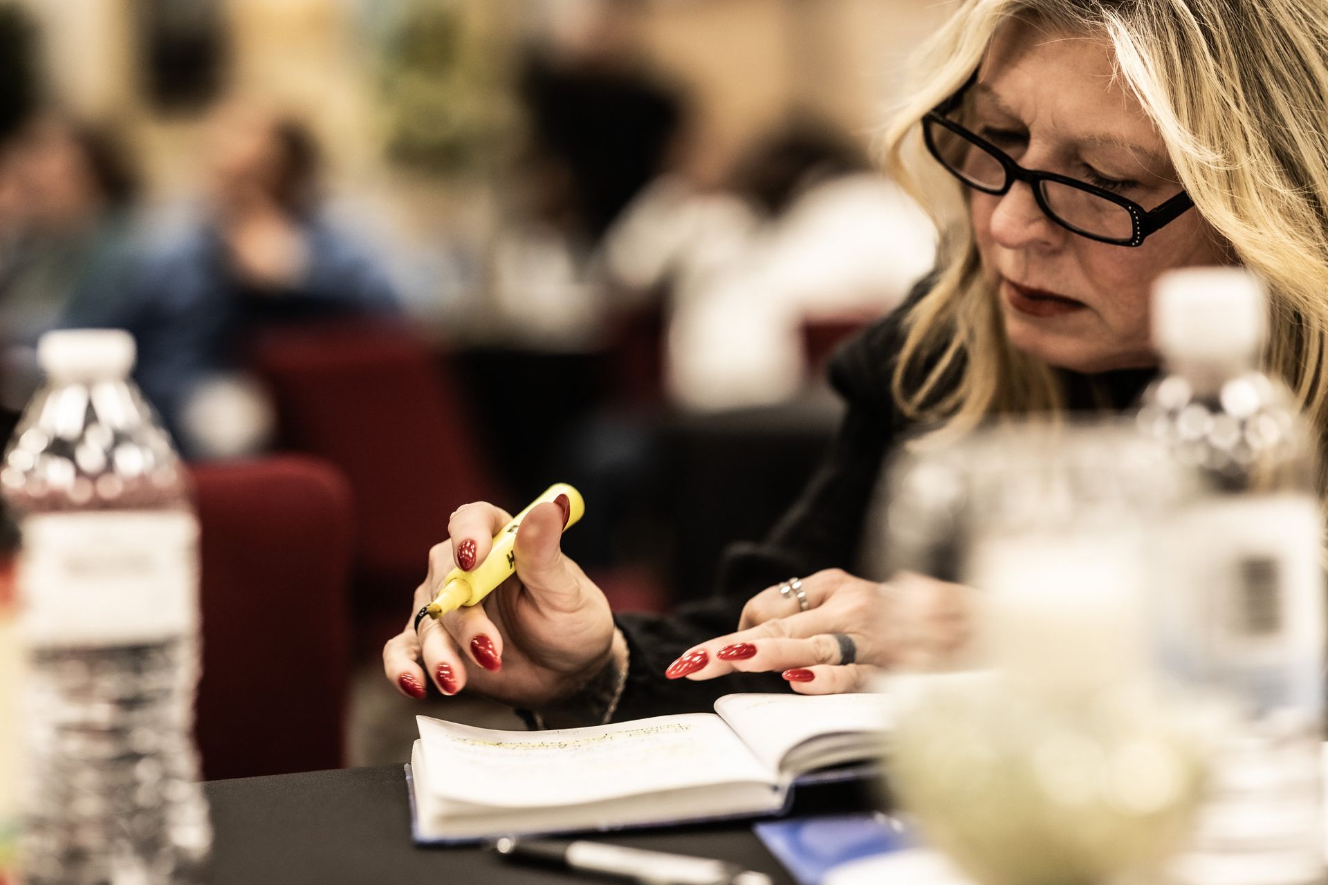A woman is sitting at a table holding a pair of scissors.