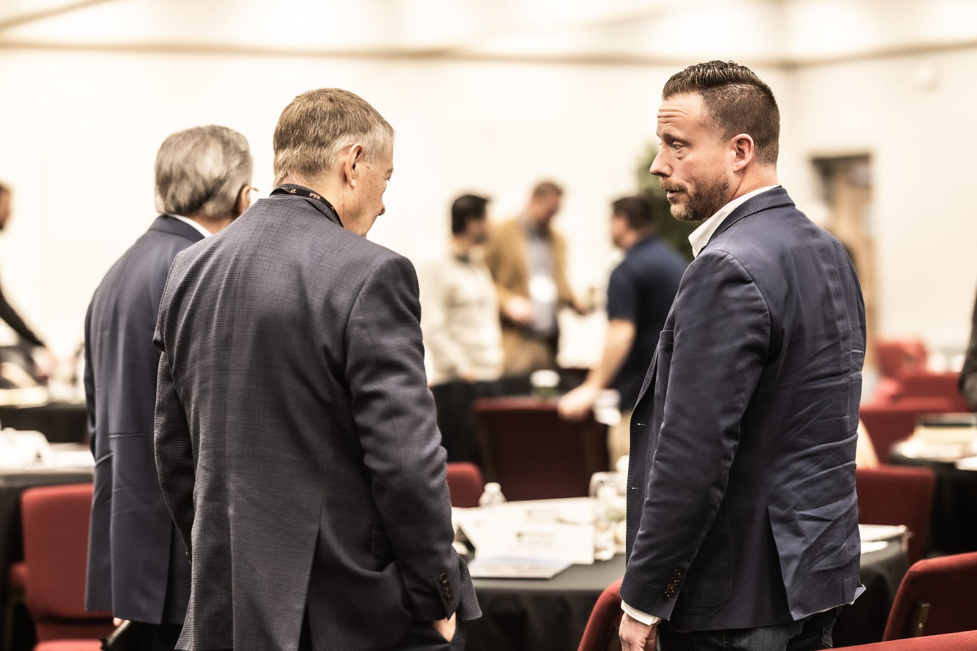 A group of men are standing in a room talking to each other.