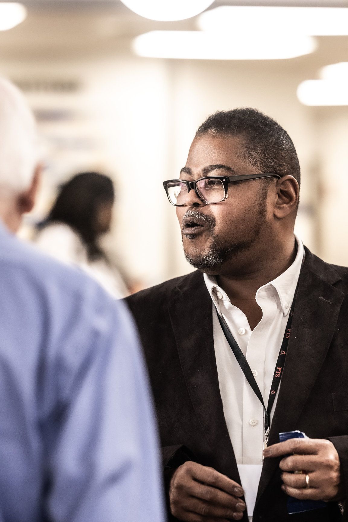 A man in a suit and glasses is talking to another man.