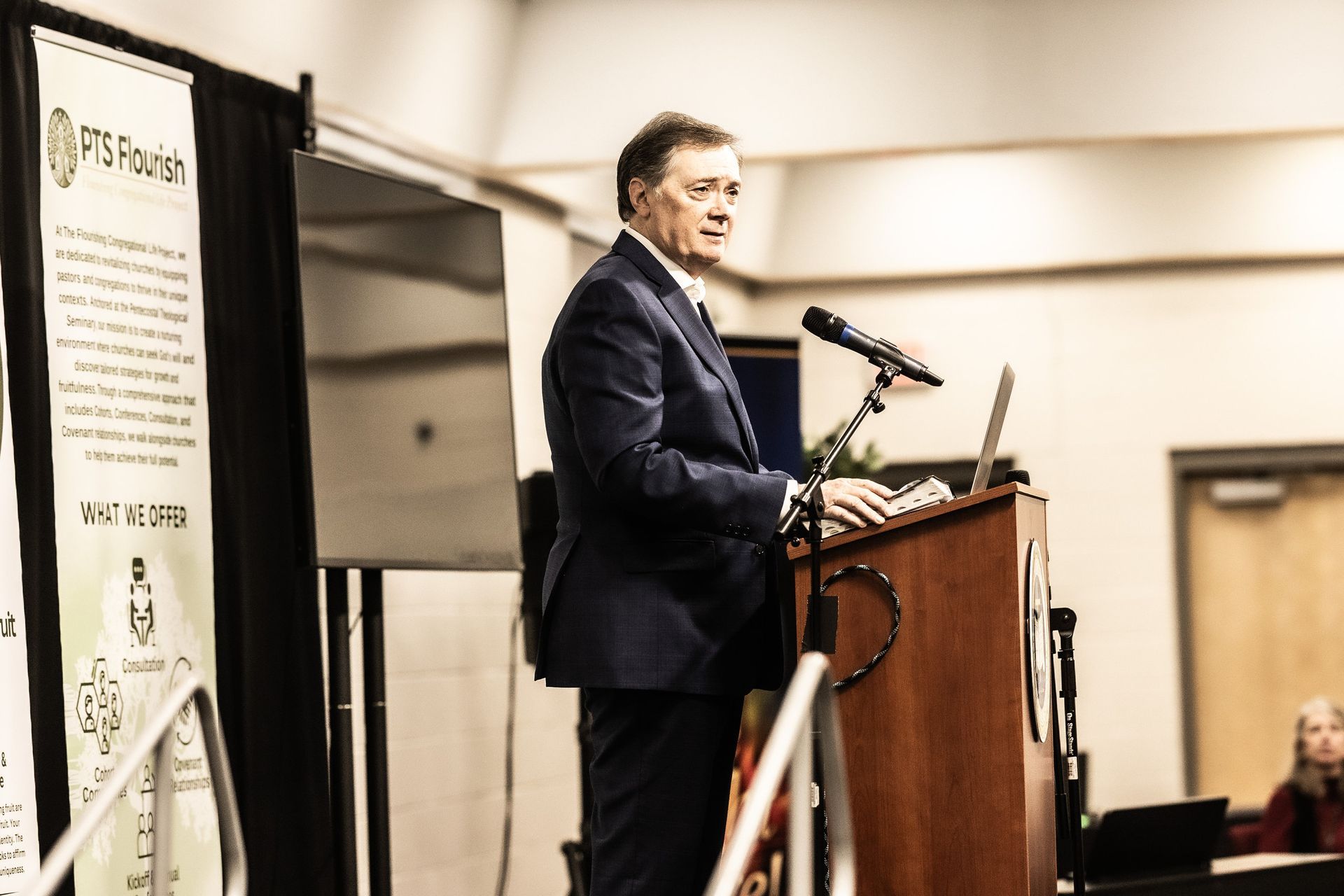 A man in a suit is standing at a podium speaking into a microphone.