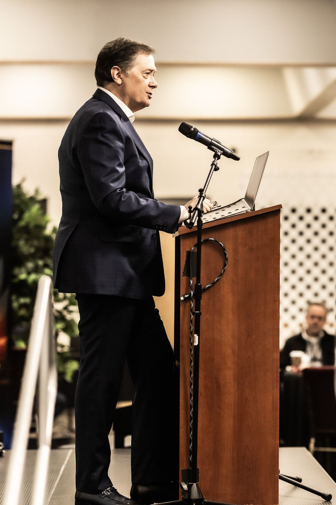 A man in a suit is standing at a podium speaking into a microphone