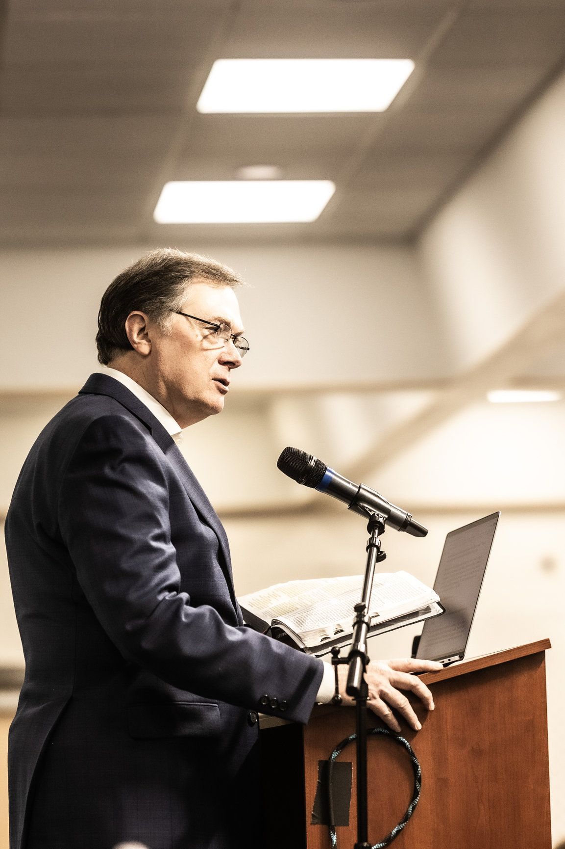 A man in a suit is standing at a podium with a microphone and a laptop.