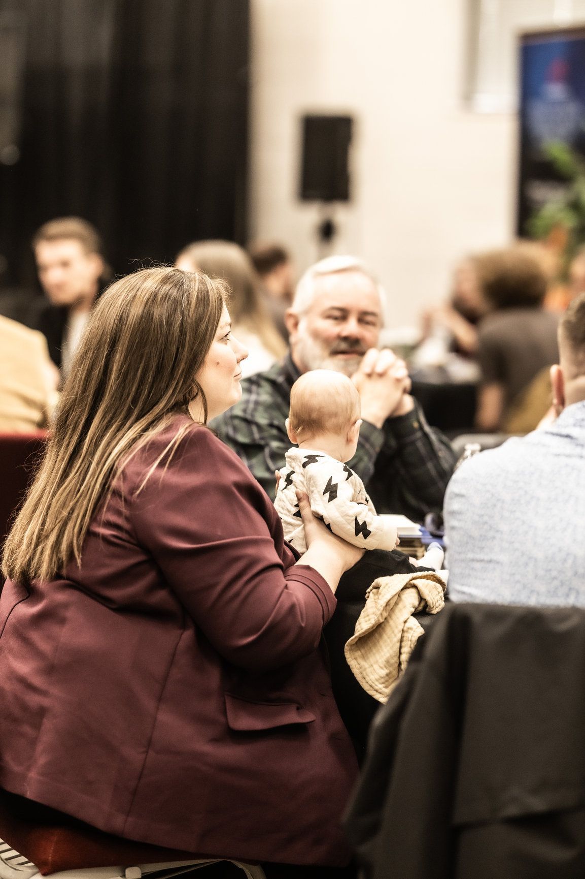 A woman is holding a baby while sitting at a table with other people.