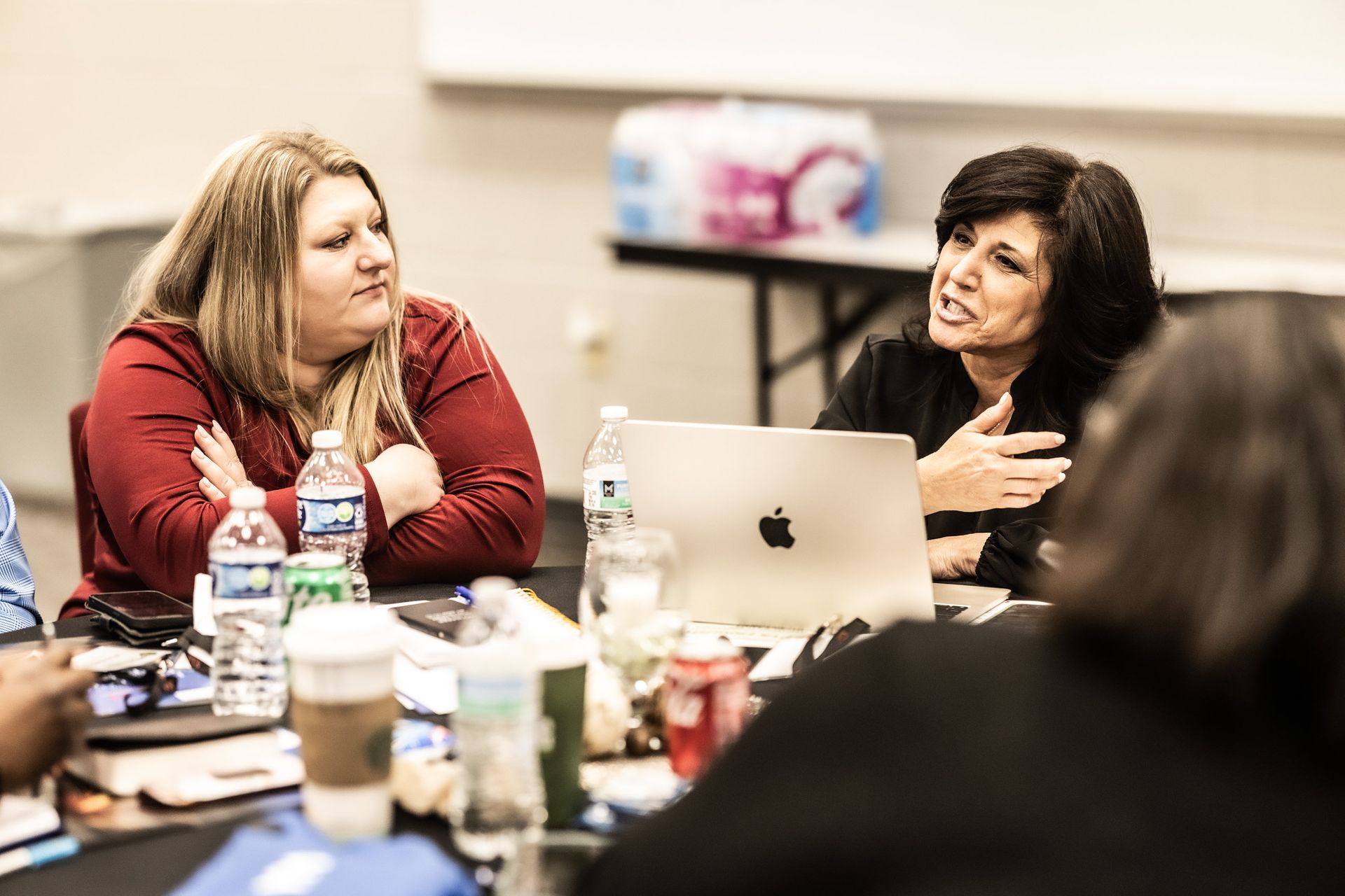 A group of women are sitting around a table with a laptop.