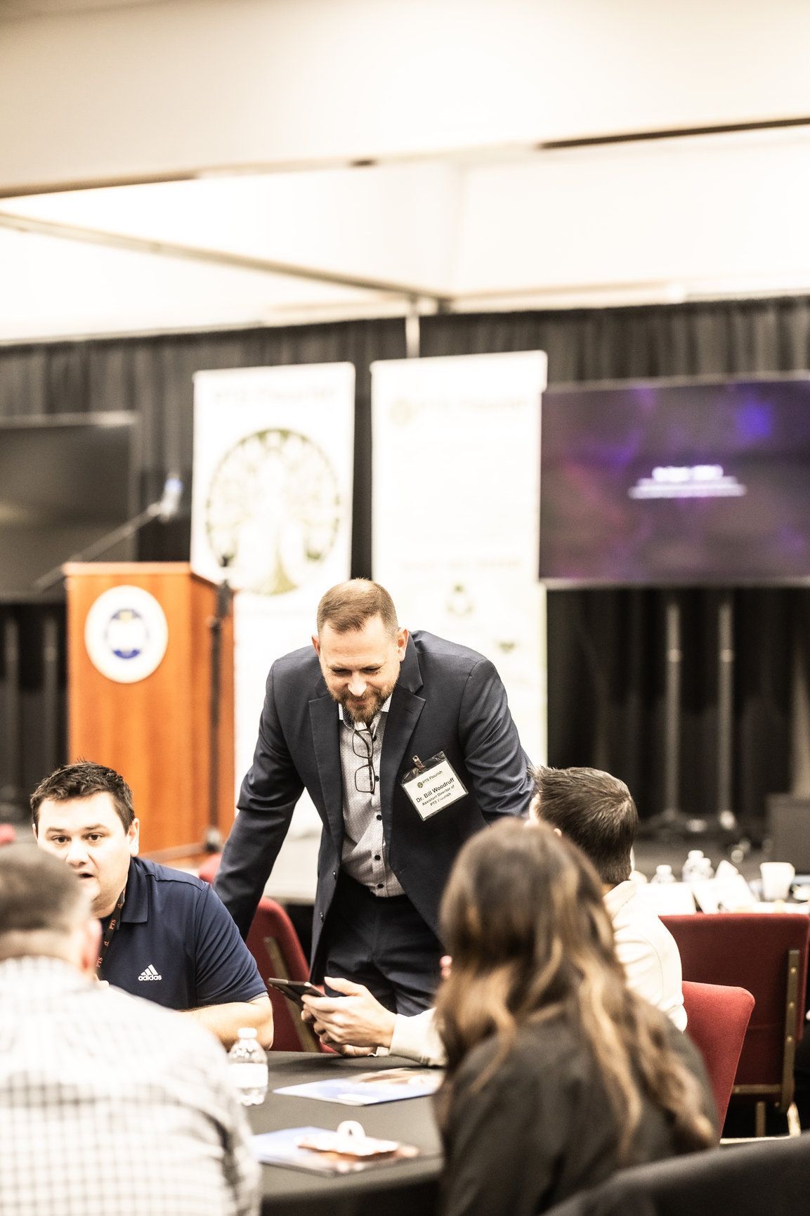 A man in a suit is standing in front of a group of people at a table.