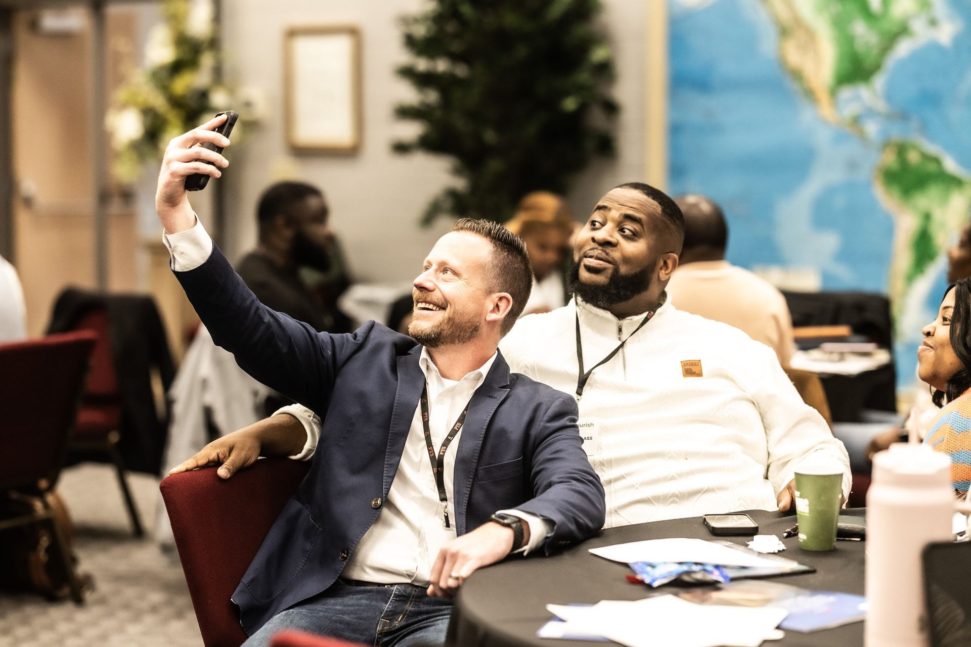 Two men are sitting at a table taking a selfie.