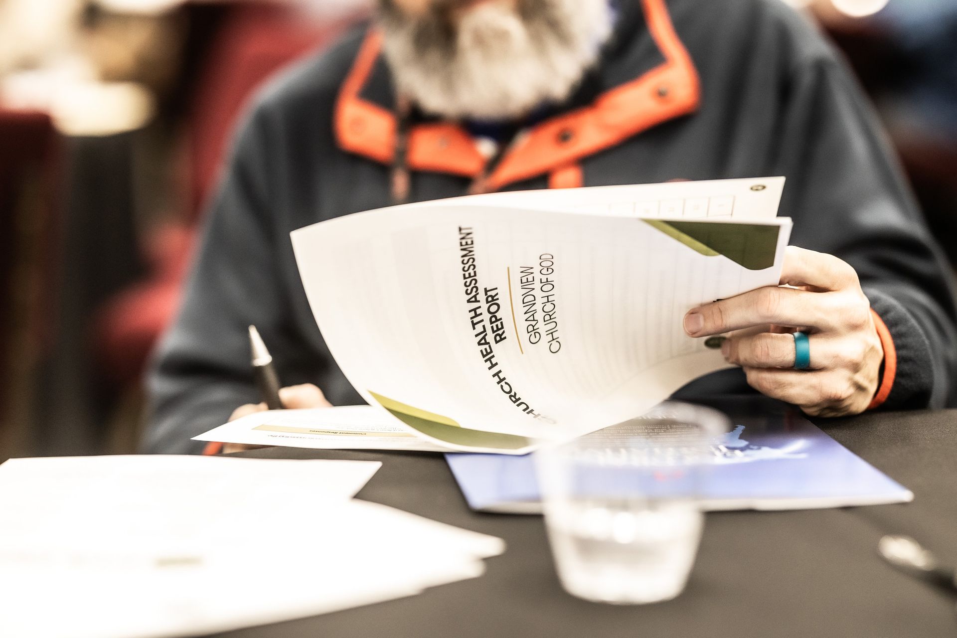 A man with a beard is sitting at a table reading a book.