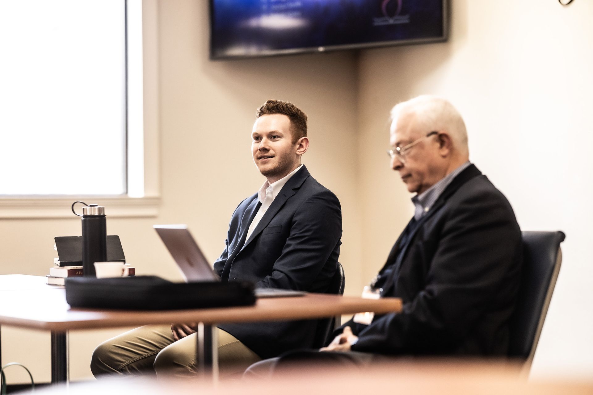 Two men are sitting at a table with a laptop.