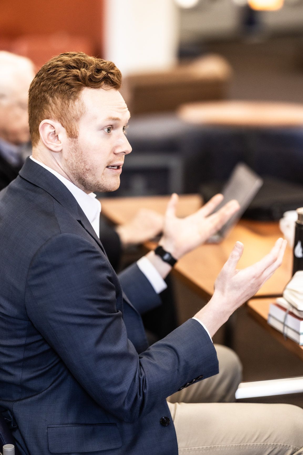 A man in a suit is sitting at a table with his hands outstretched.