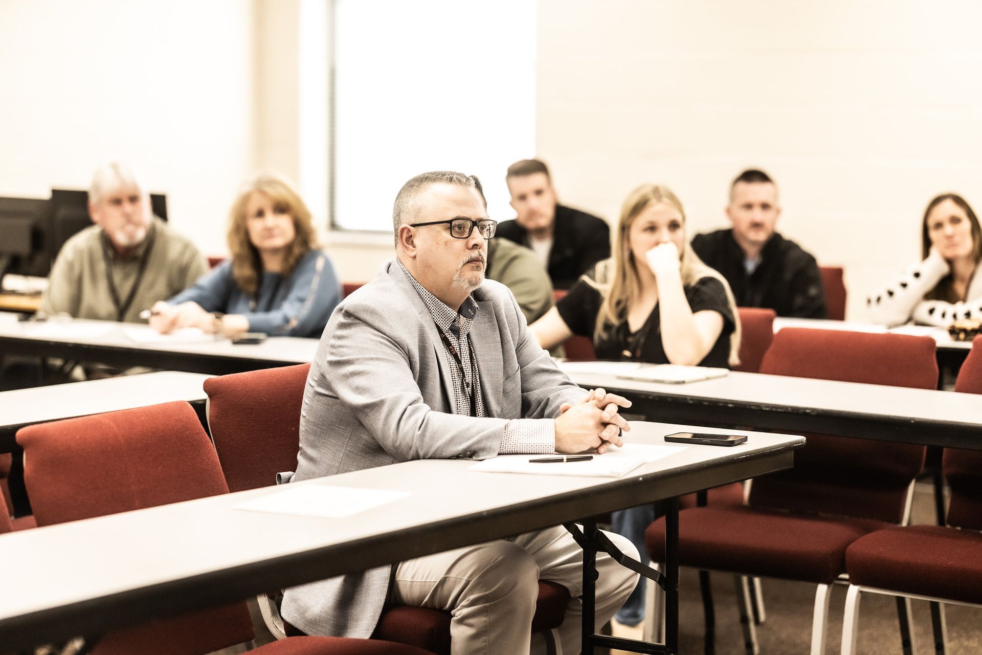 A group of people are sitting at tables in a classroom.