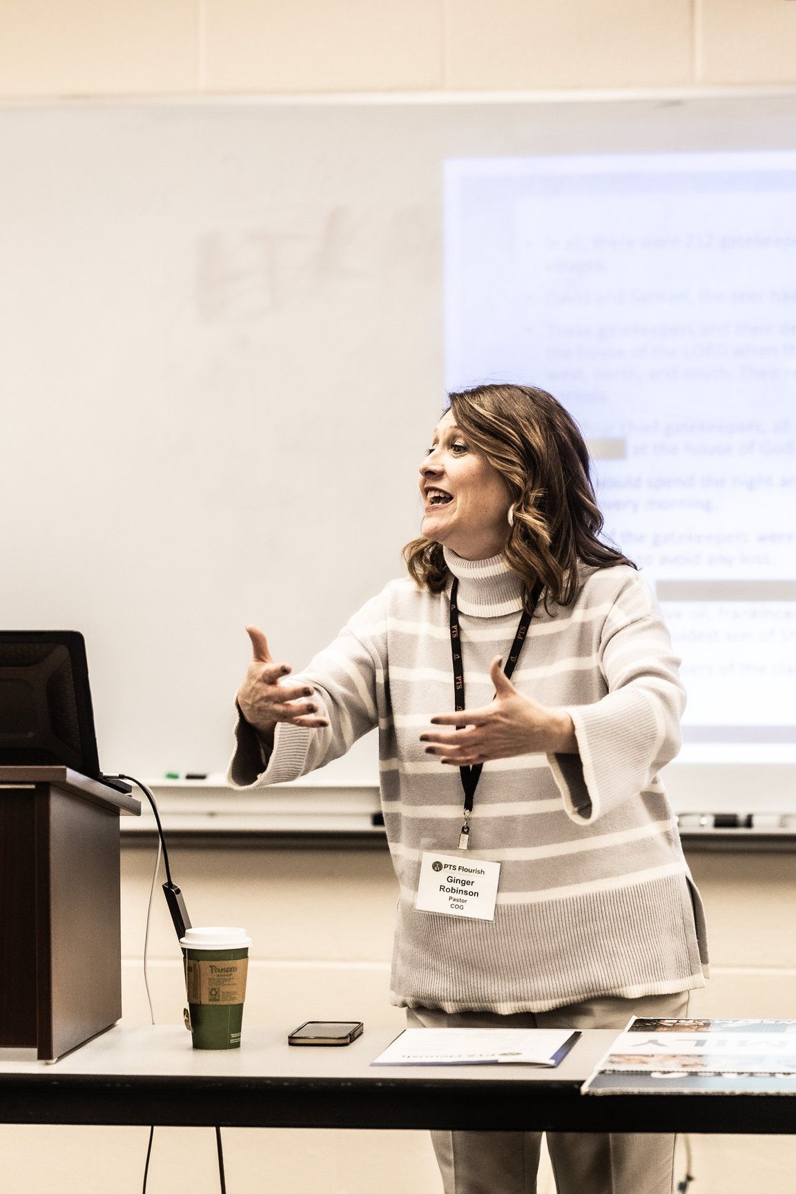A woman is standing at a podium giving a presentation in a classroom.