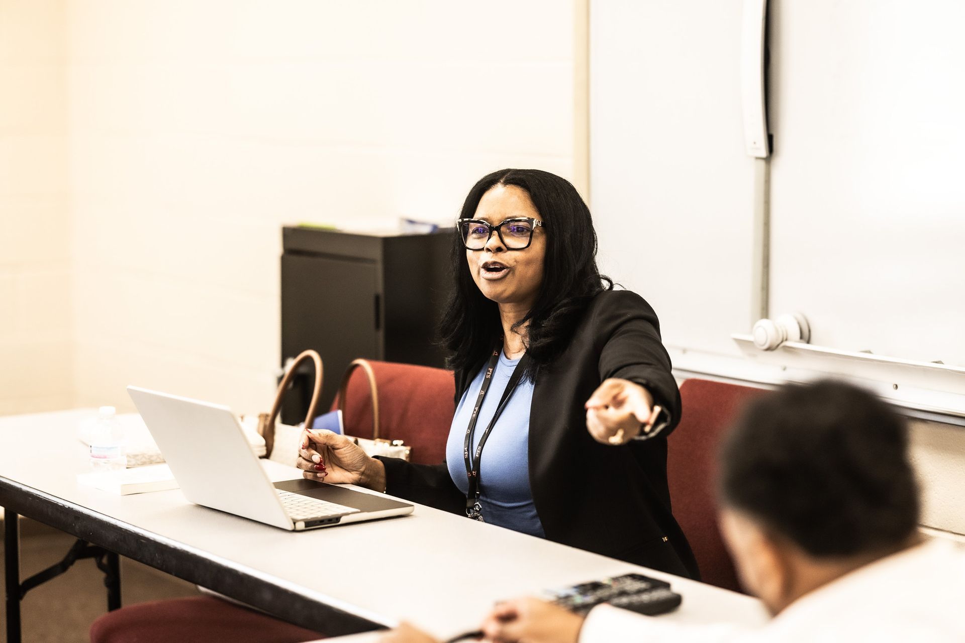 A woman is sitting at a table with a laptop and talking to a group of people.