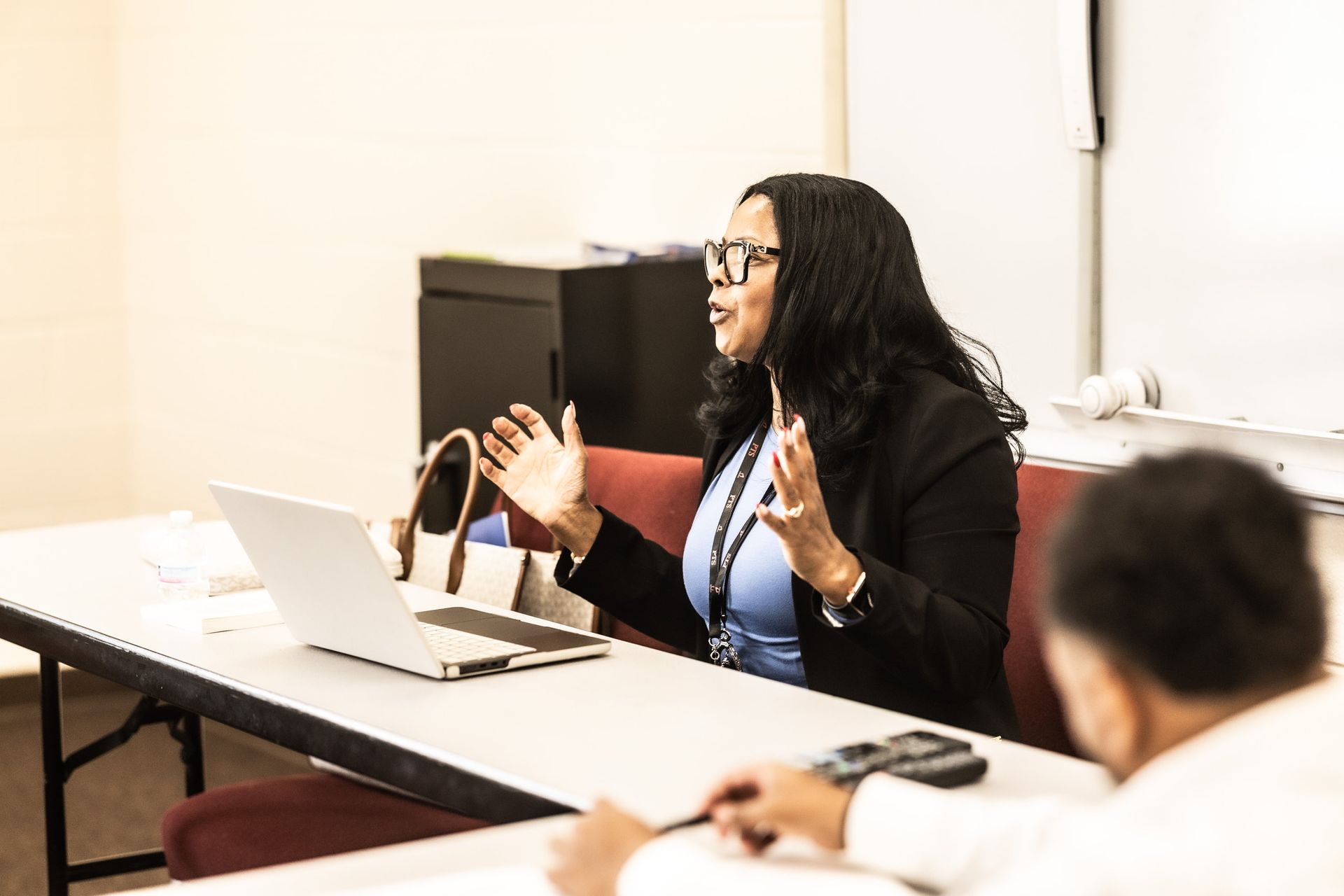 A woman is sitting at a table with a laptop and talking to a group of people.