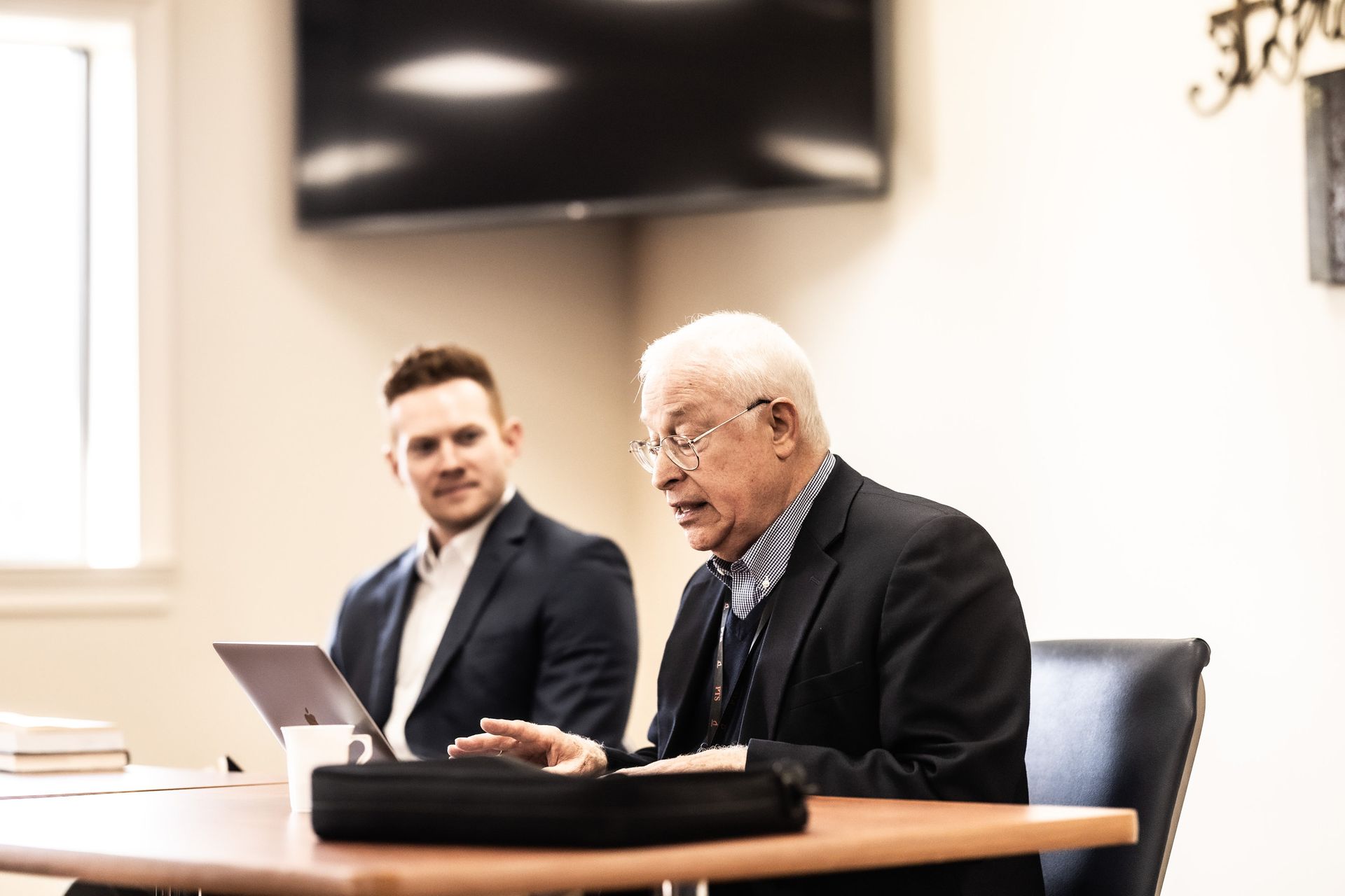 Two men are sitting at a table in a conference room.