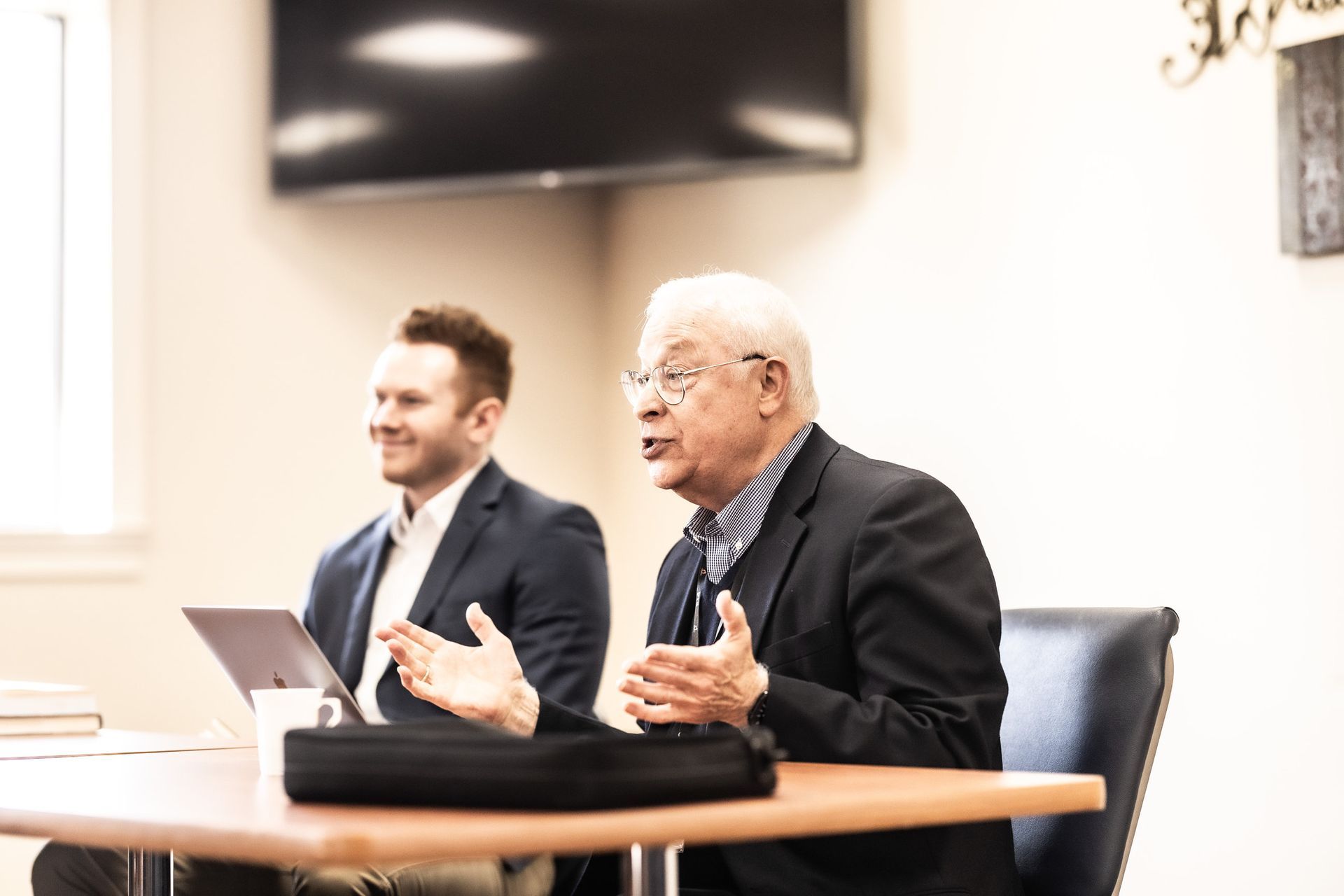 Two men are sitting at a table talking to each other.