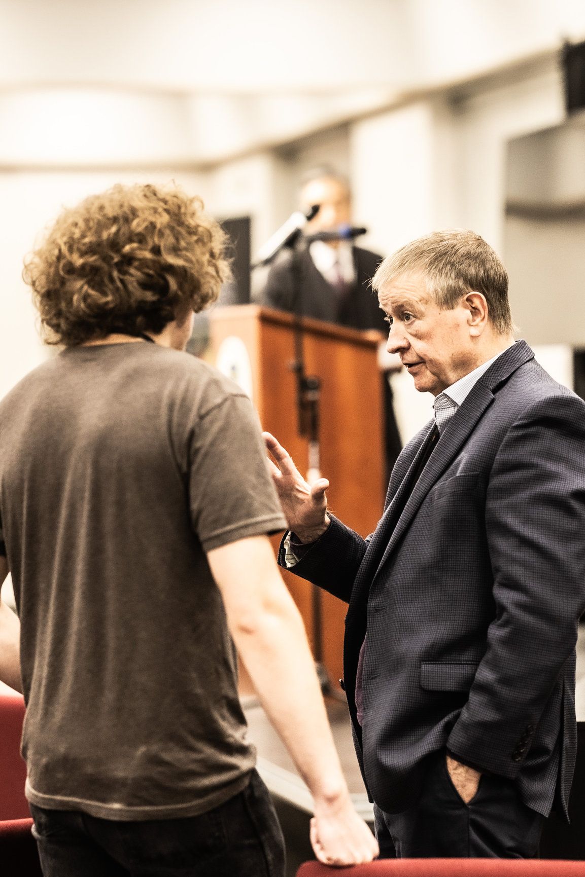 A man in a suit is talking to a young man in a brown shirt.