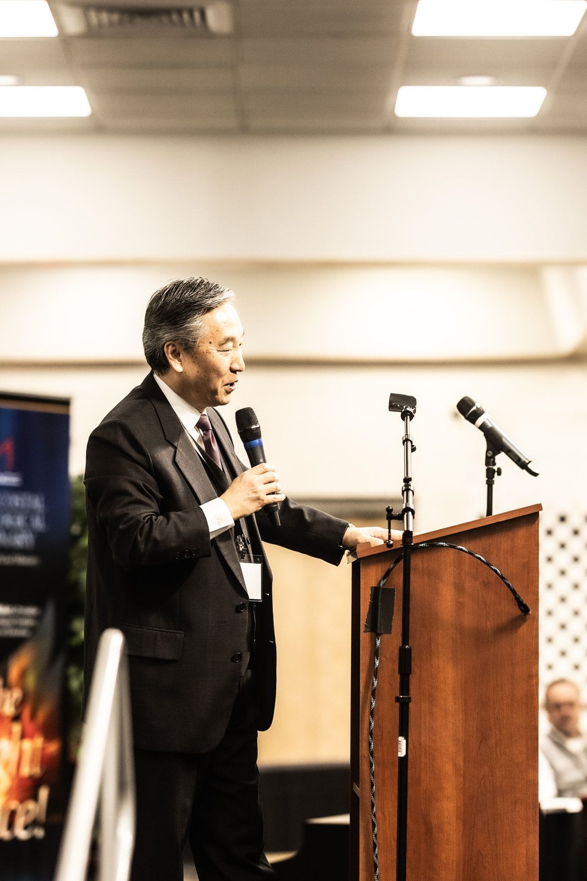 A man in a suit and tie is speaking into a microphone at a podium