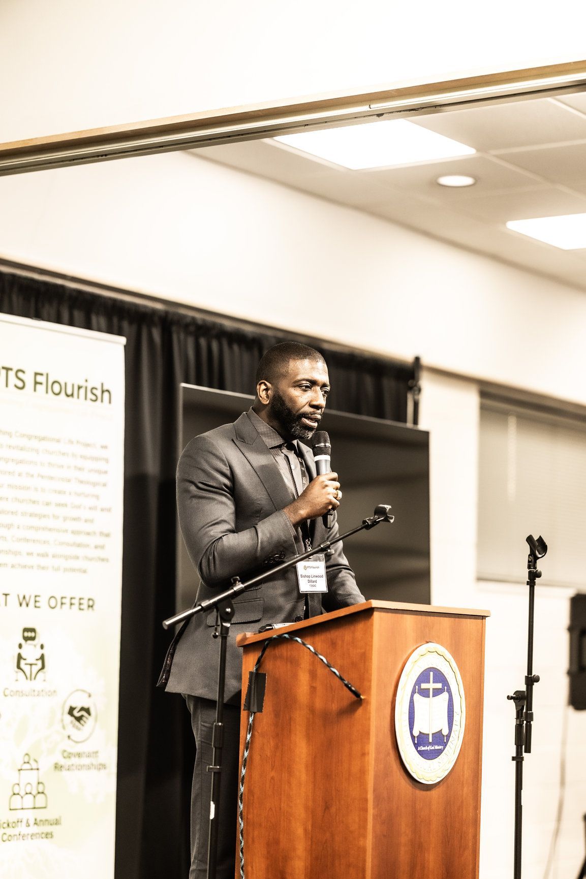 A man in a suit is standing at a podium holding a microphone.