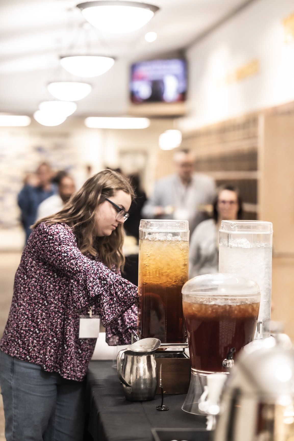 A woman is pouring a drink from a dispenser at a table.