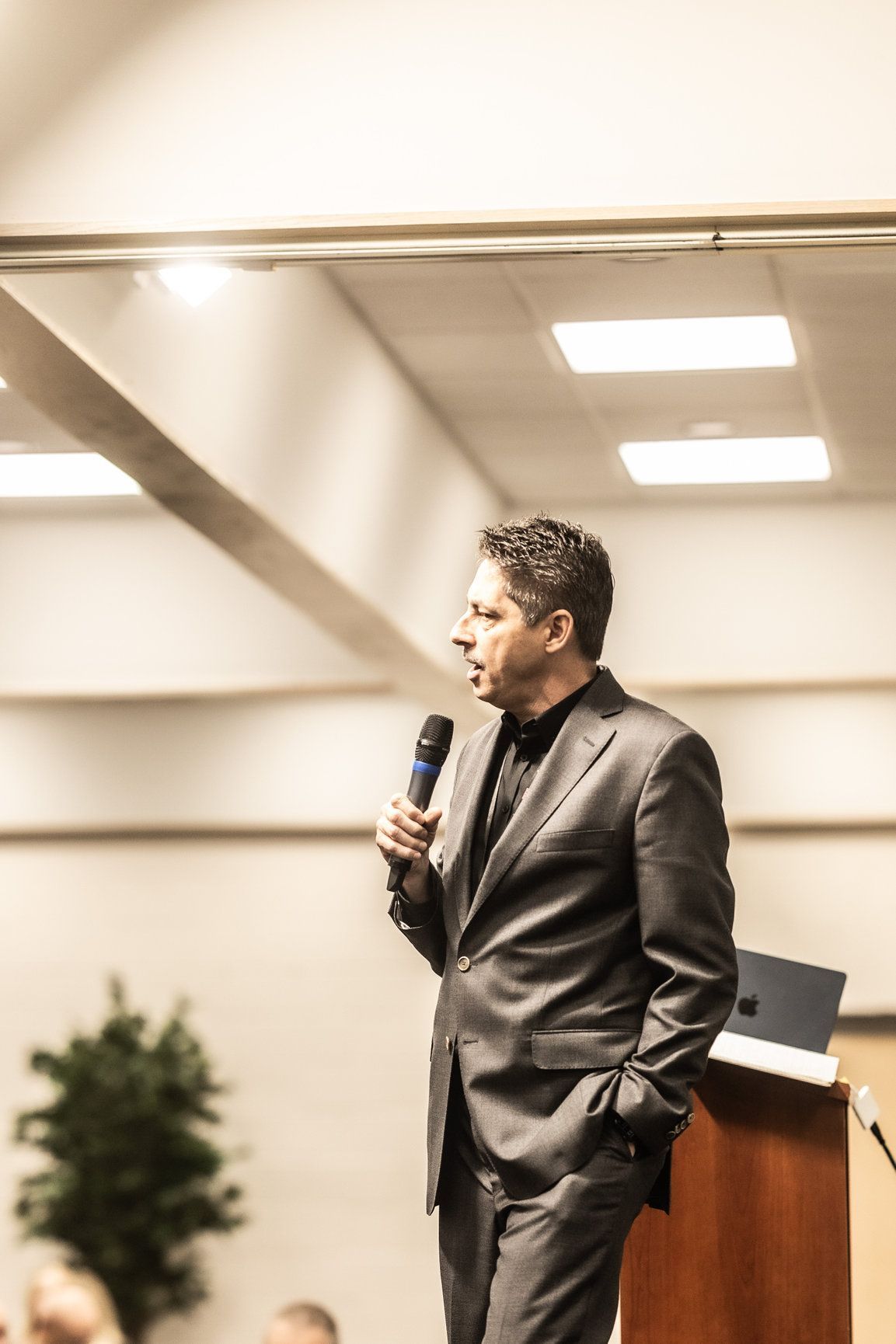 A man in a suit is standing at a podium holding a microphone.