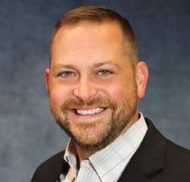 A man with a beard is wearing a suit and smiling for the camera.