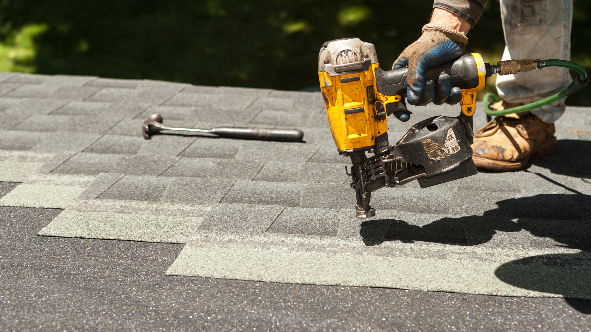 Worker using a yellow nail gun to fasten shingles on a rooftop