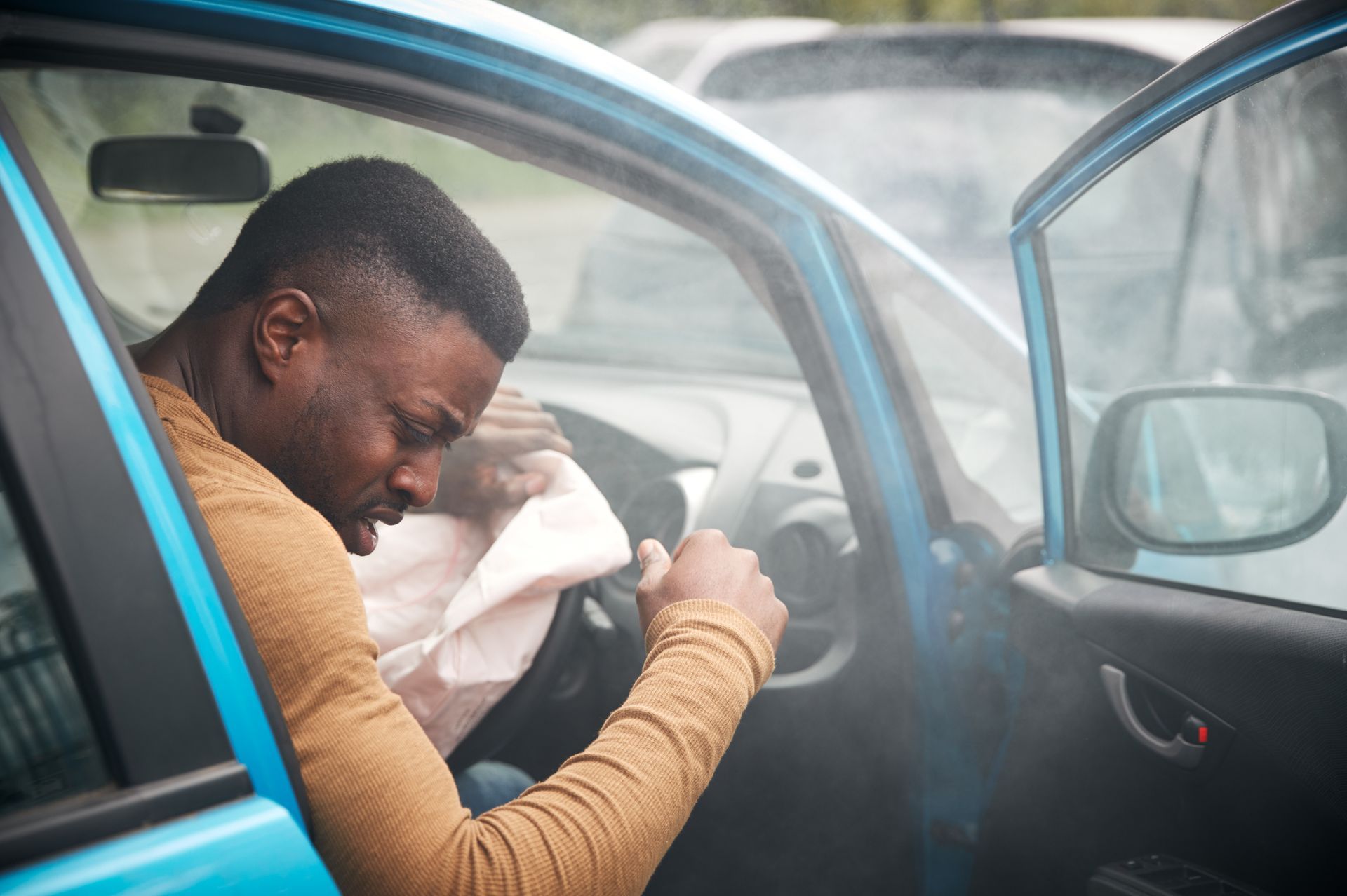 man getting out of car distraught, smoke surrounds his car