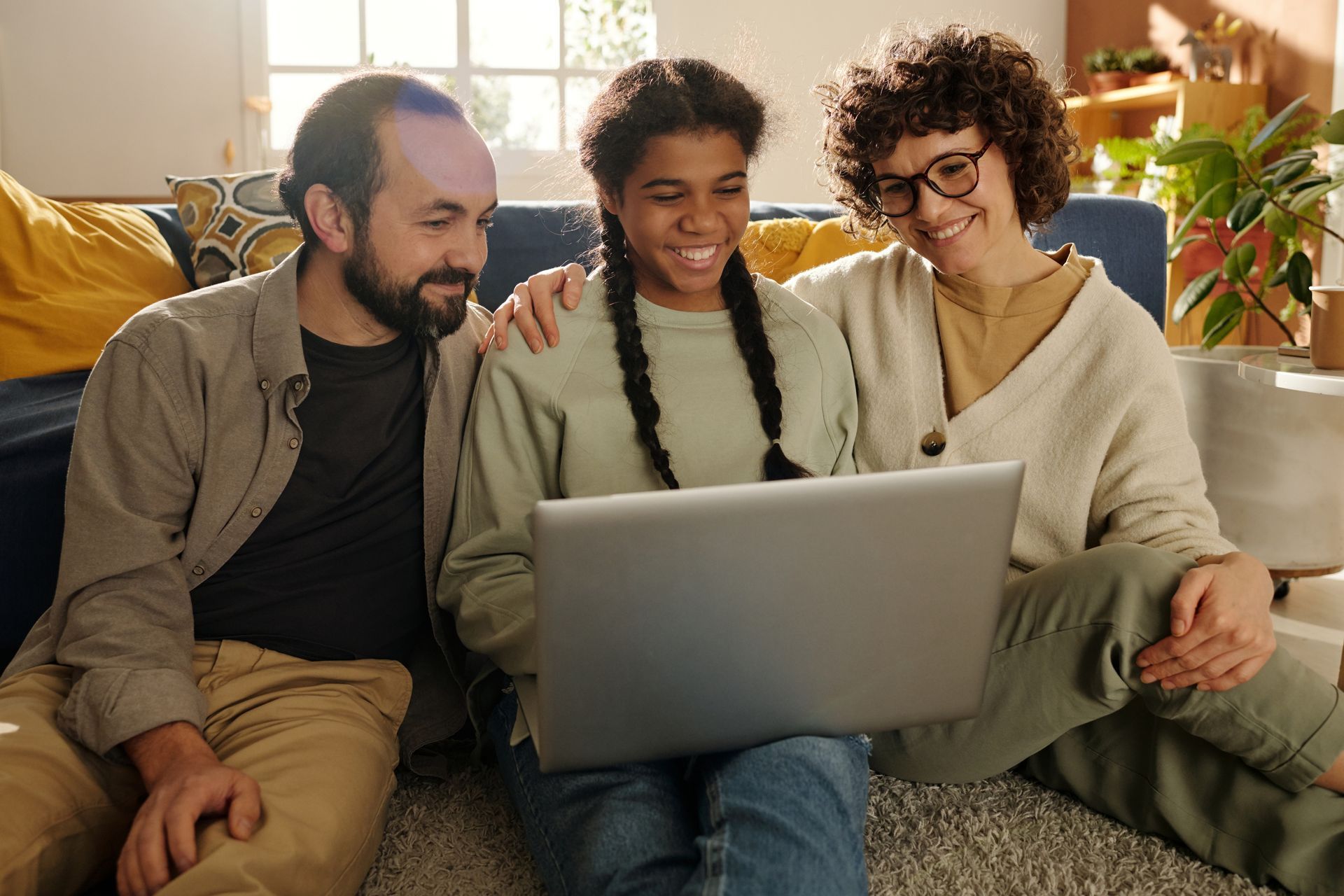 two adults sitting on either side of a young adult, they're smiling together looking at a laptop