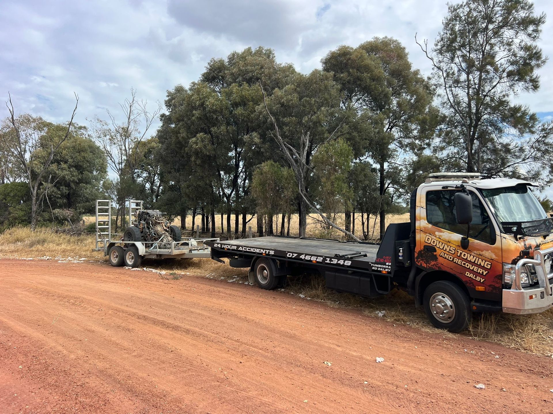Orange Flatbed Truck Hauling Equipment On A Dirt Road Beside Trees — Downs Towing & Recovery Service in Miles, QLD
