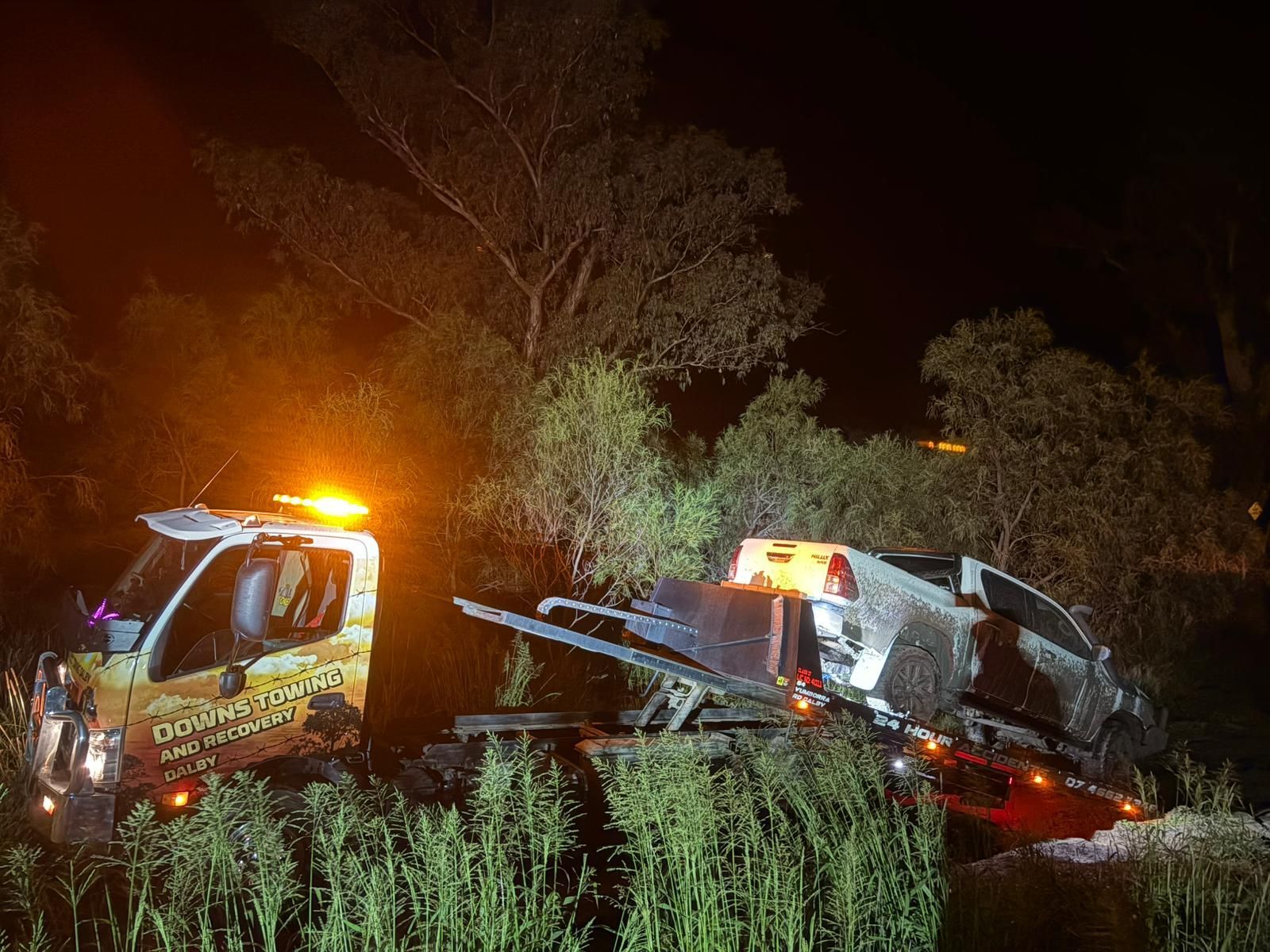 Two Tow Trucks Recovering A Damaged Vehicle At Night In A Wooded Ditch, With Flashing Orange Lights — Downs Towing & Recovery Service in St George, QLD