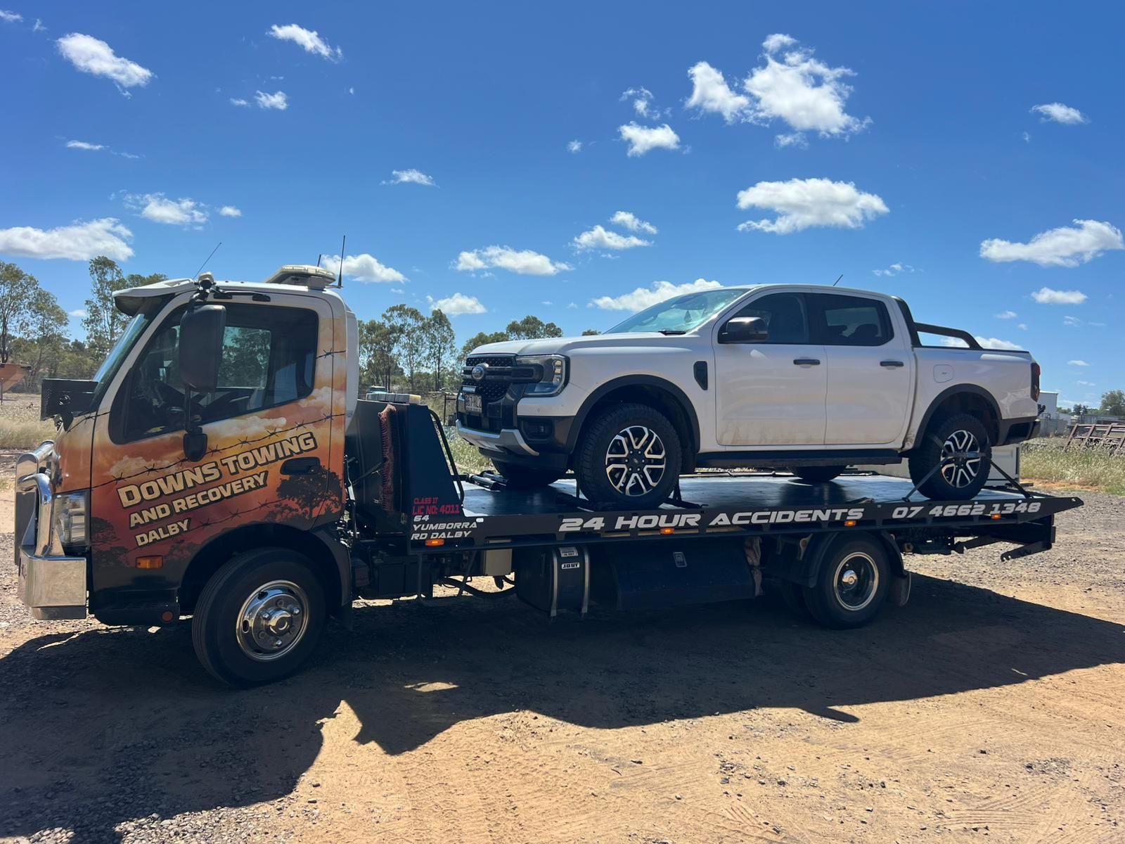 Tow Truck Carrying A White Pickup On A Flatbed Under A Bright Blue Sky With Clouds — Downs Towing & Recovery Service in Miles, QLD