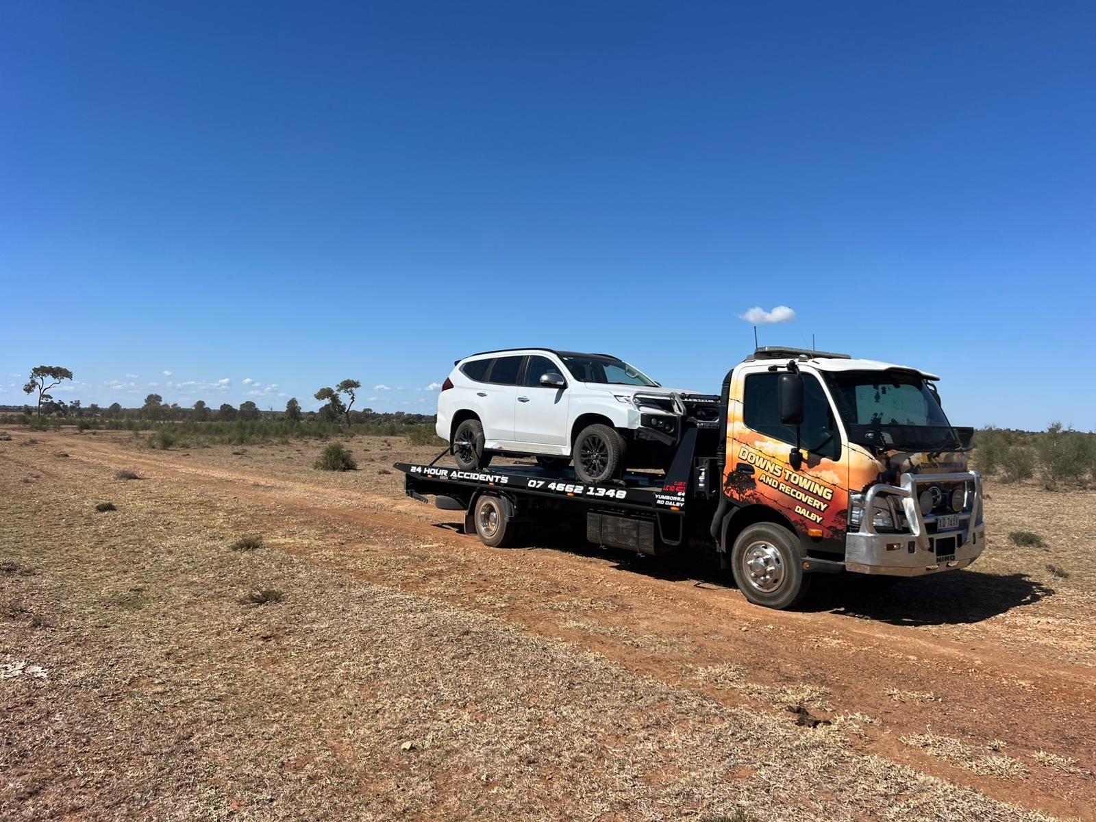 Tow Truck Hauling A White SUV Across A Dry, Open Landscape Under A Clear Blue Sky — Downs Towing & Recovery Service in St. George, QLD