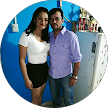 Dos personas de pie juntas en el interior de un edificio, sonriendo a la cámara, con decoraciones azules de fondo.