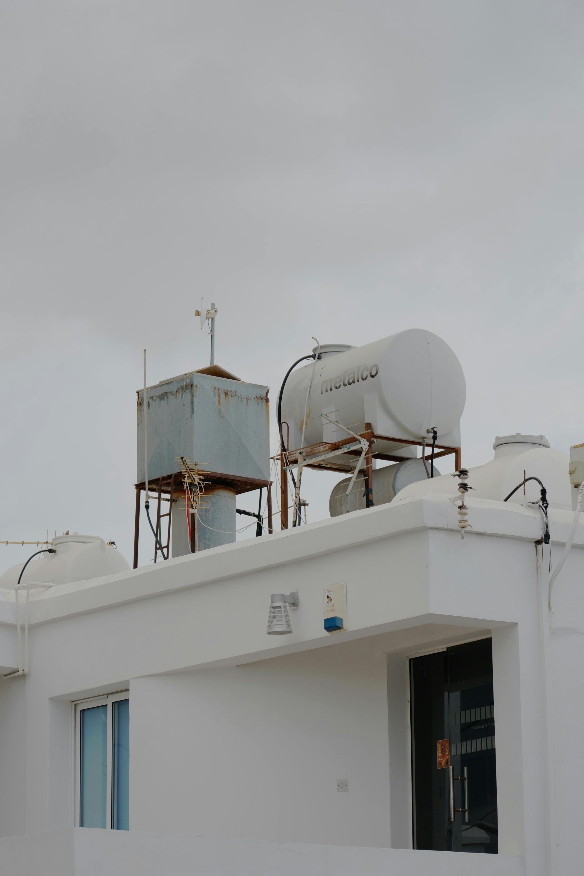 Azotea blanca con tanques de agua y equipos de servicios públicos bajo un cielo gris.