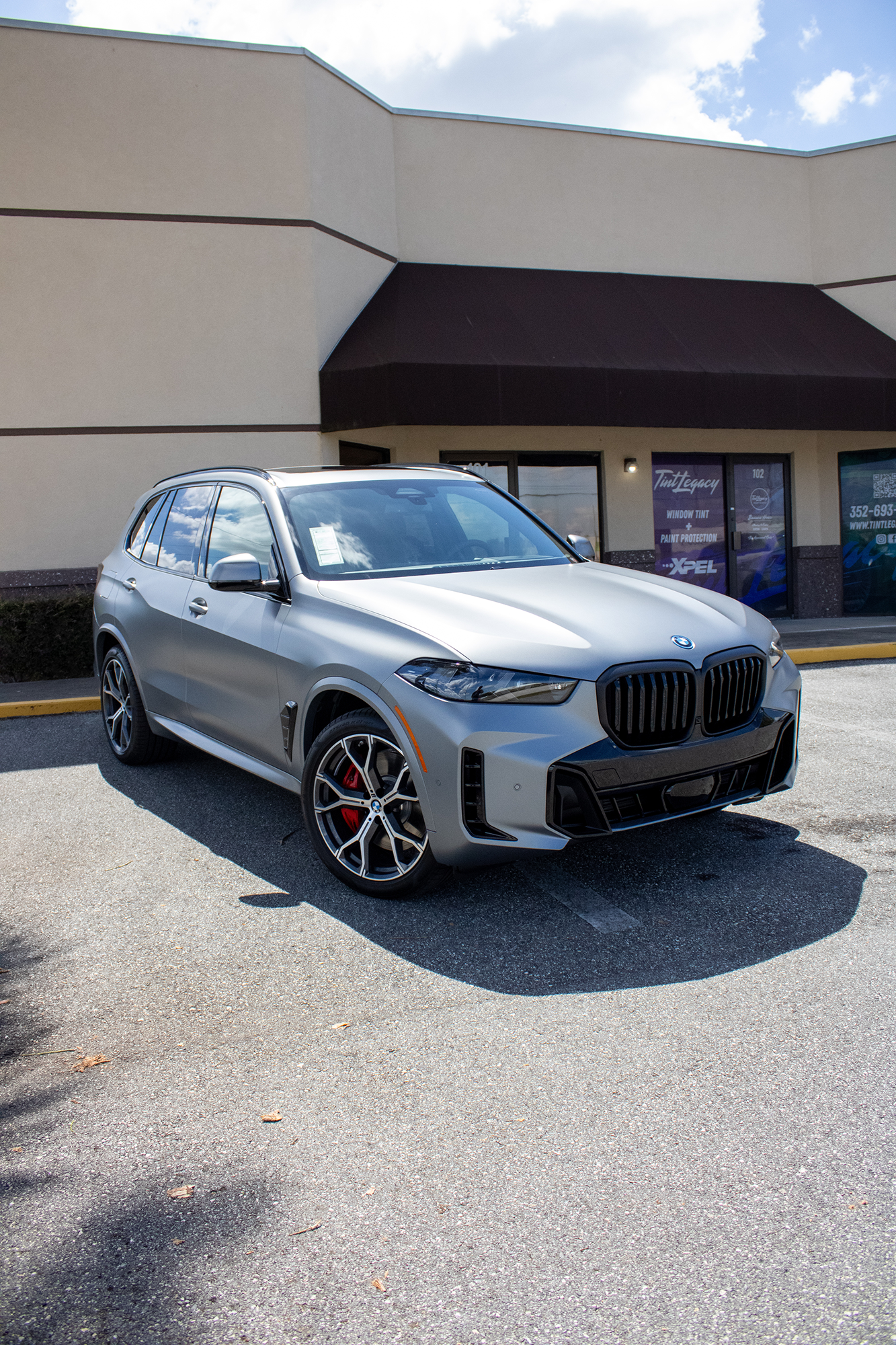 Silver BMW SUV parked outside a storefront on a sunny day