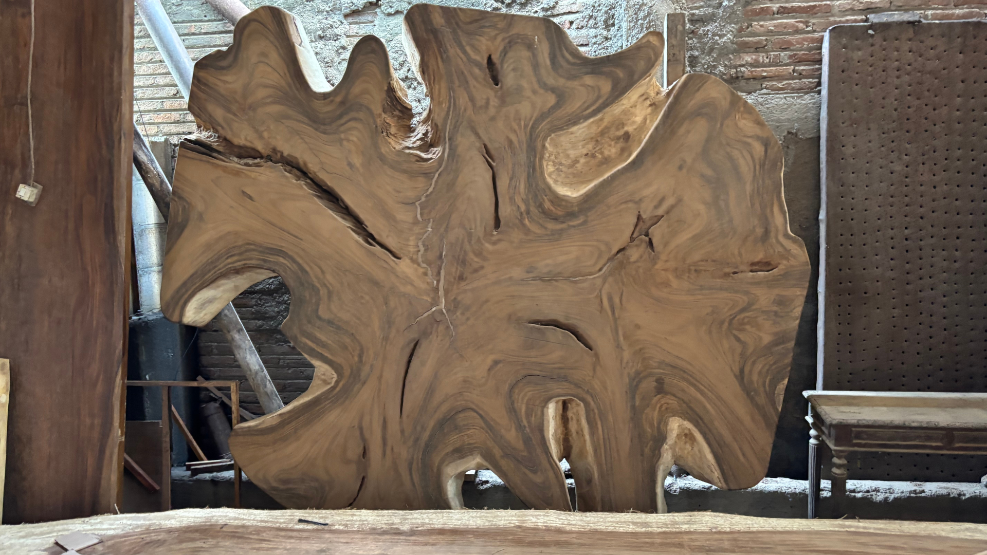 Large carved wood slab with swirling grain leaned against a wall beside patio chairs in an outdoor setting