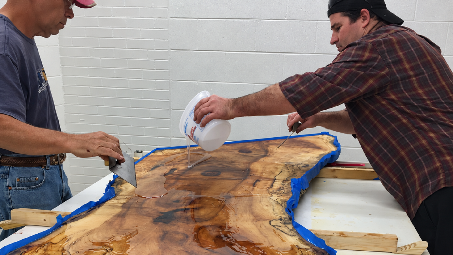 Two men pour resin onto a large wood slab on a worktable in a workshop, work of Specialty Slabwood Creations