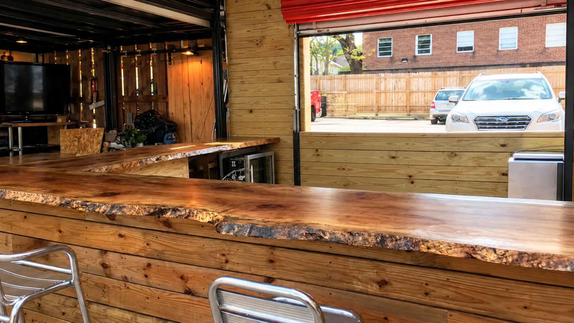 Empty wooden bar counter in an open-air café with brick walls and parked cars outside.