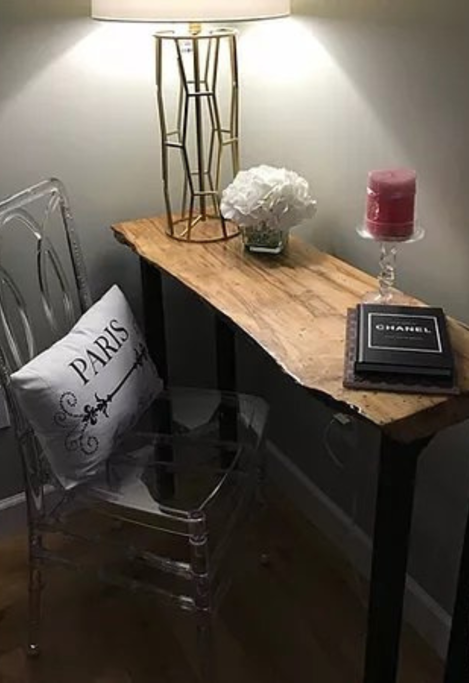 Small entryway table with lamp, decor, candle, and clear chair beside a pillow reading “Paris”