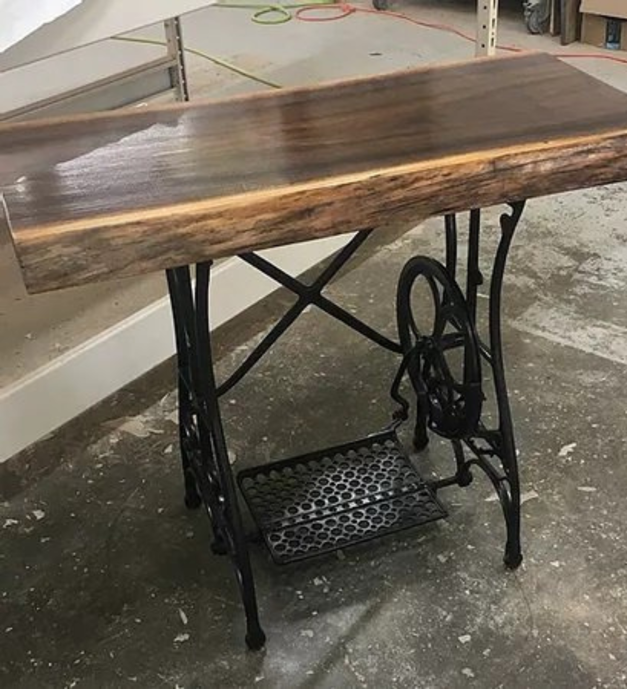 Rustic wood-top sewing table with black cast-iron treadle base on a concrete floor