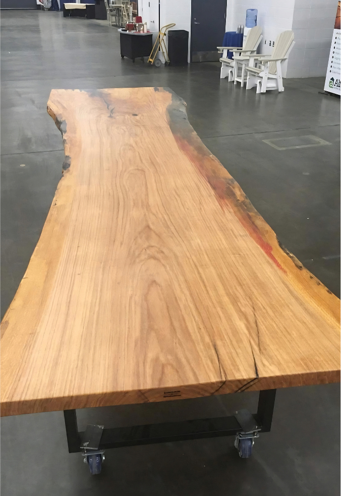 Live-edge wood table on wheels in a showroom with a dark tiled floor and white chairs in the background