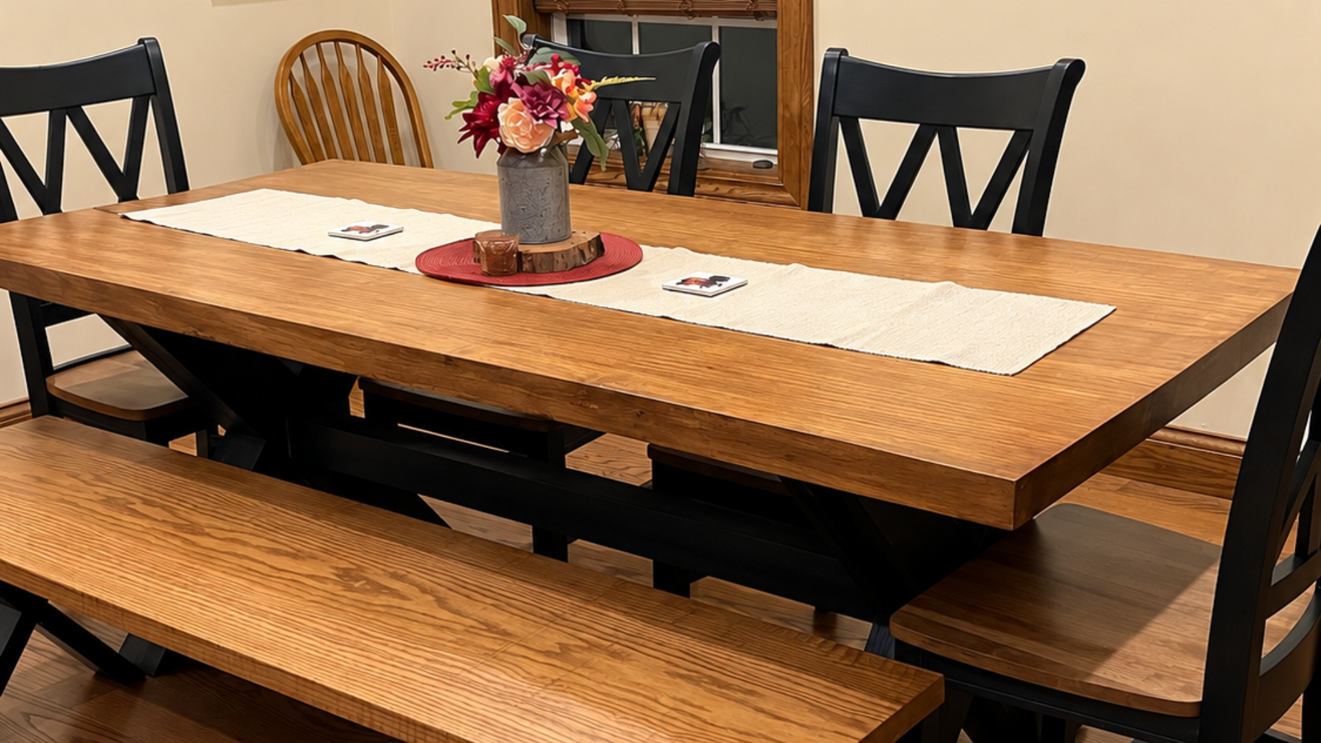 Wooden dining table with bench seating, black chairs, and a vase of flowers on a beige table runner, work of Specialty Slabwood Creations