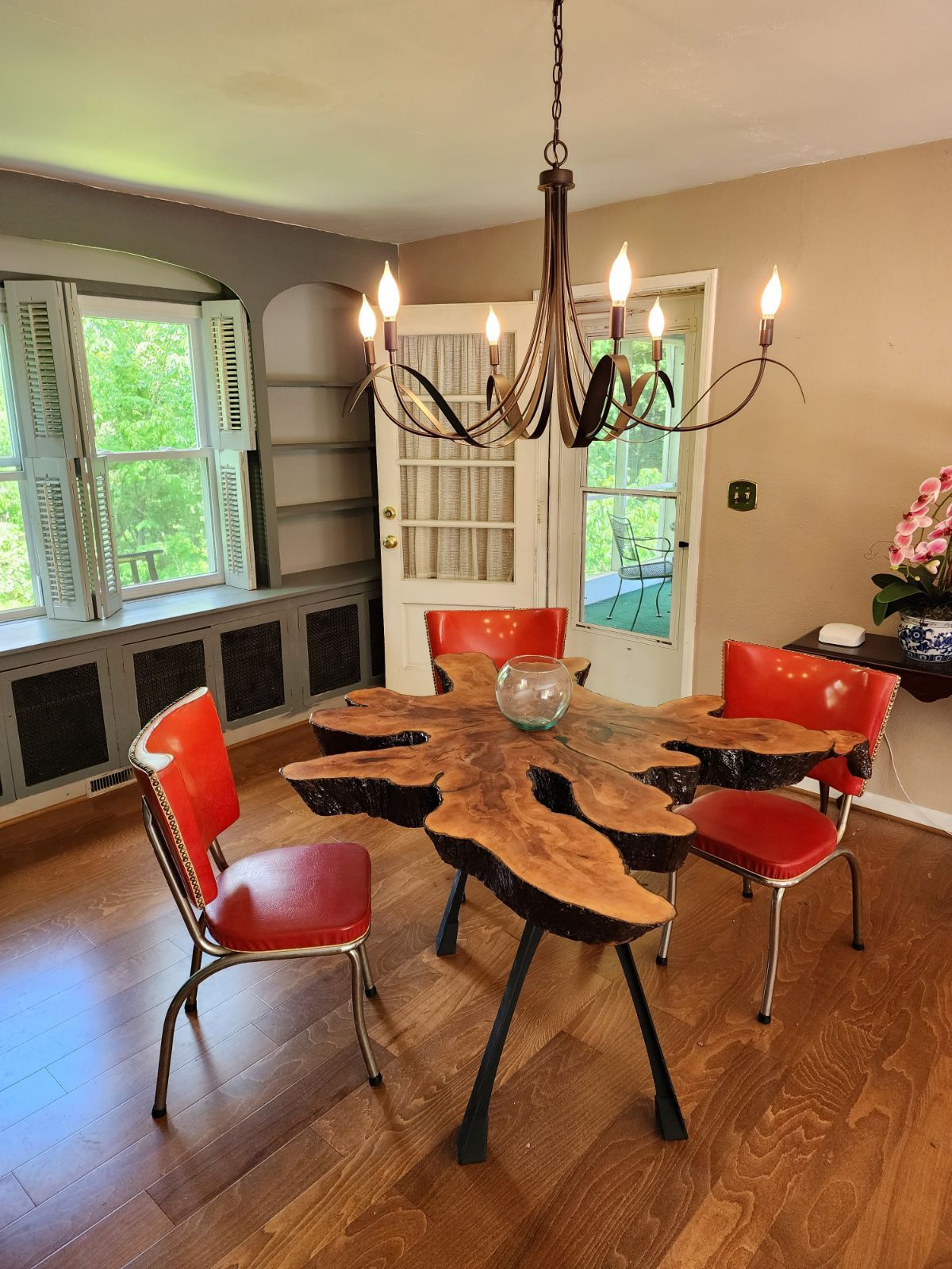 Dining room with a wood slab table, red chairs, chandelier, and white French doors to a garden.