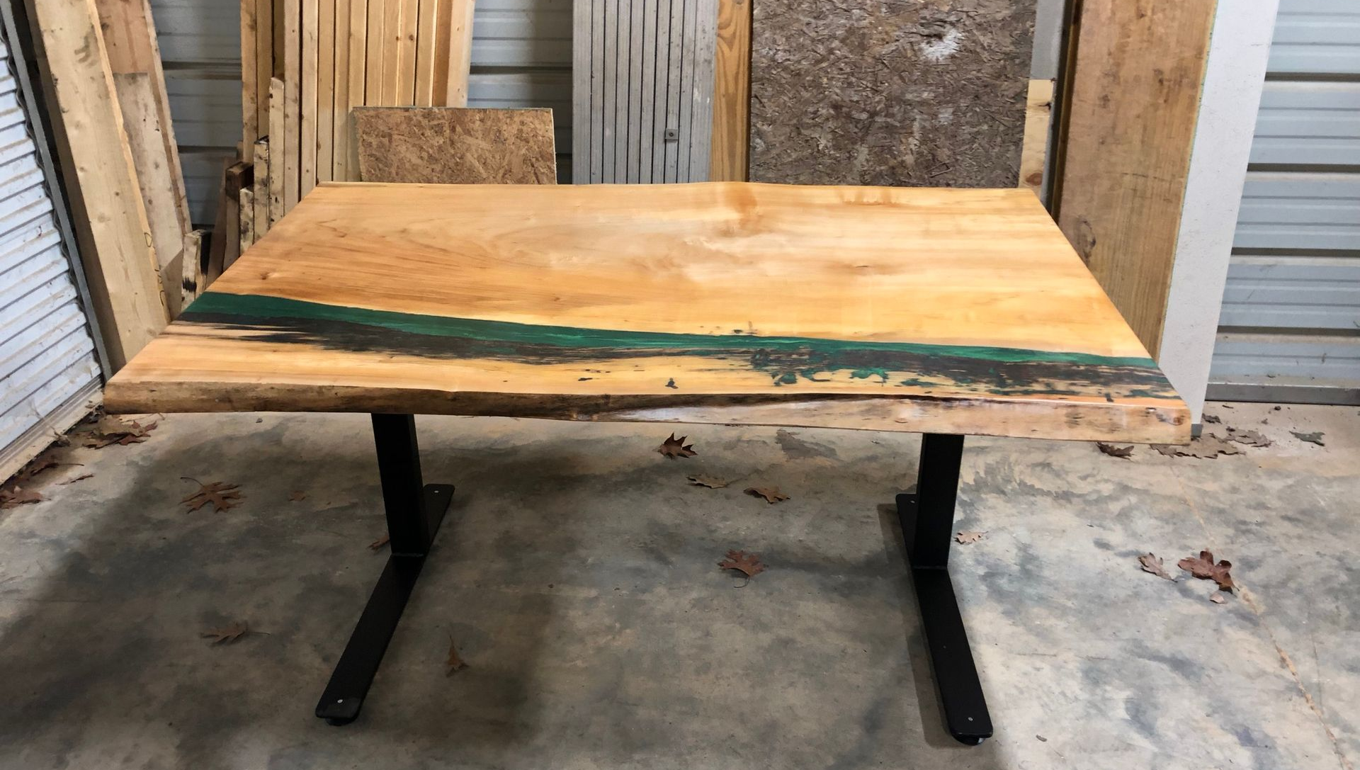 Wooden tabletop with a dark green resin stripe on black metal legs, outdoors in a workshop area